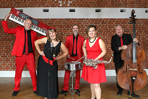 Hochzeitsmusik-Oberösterreich, Hochzeitsband Voices And Music, Liveband in Österreich, Quintett, 5 Musikerinnen, Sängerinnen, Sänger, Saxofon, Keyboard, Schlagzeug, Kontrabass, rote und schwarze Kleidung, rote Ziegelwand im Hintergrund,